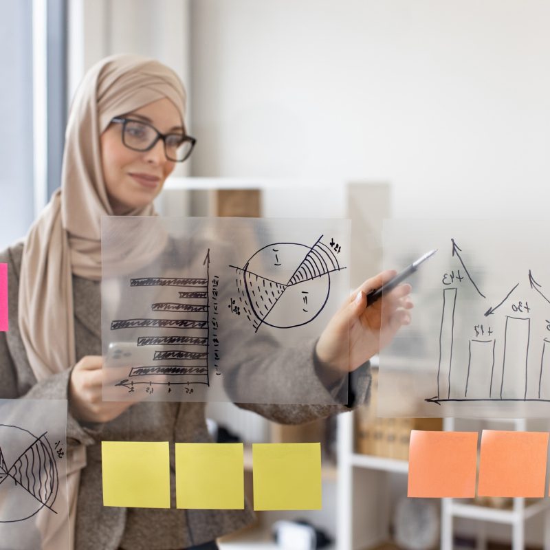 Muslim woman holding smartphone and looking on financial graphic.