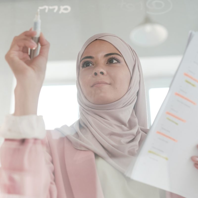 Young serious female broker in hijab holding financial papers and highlighter